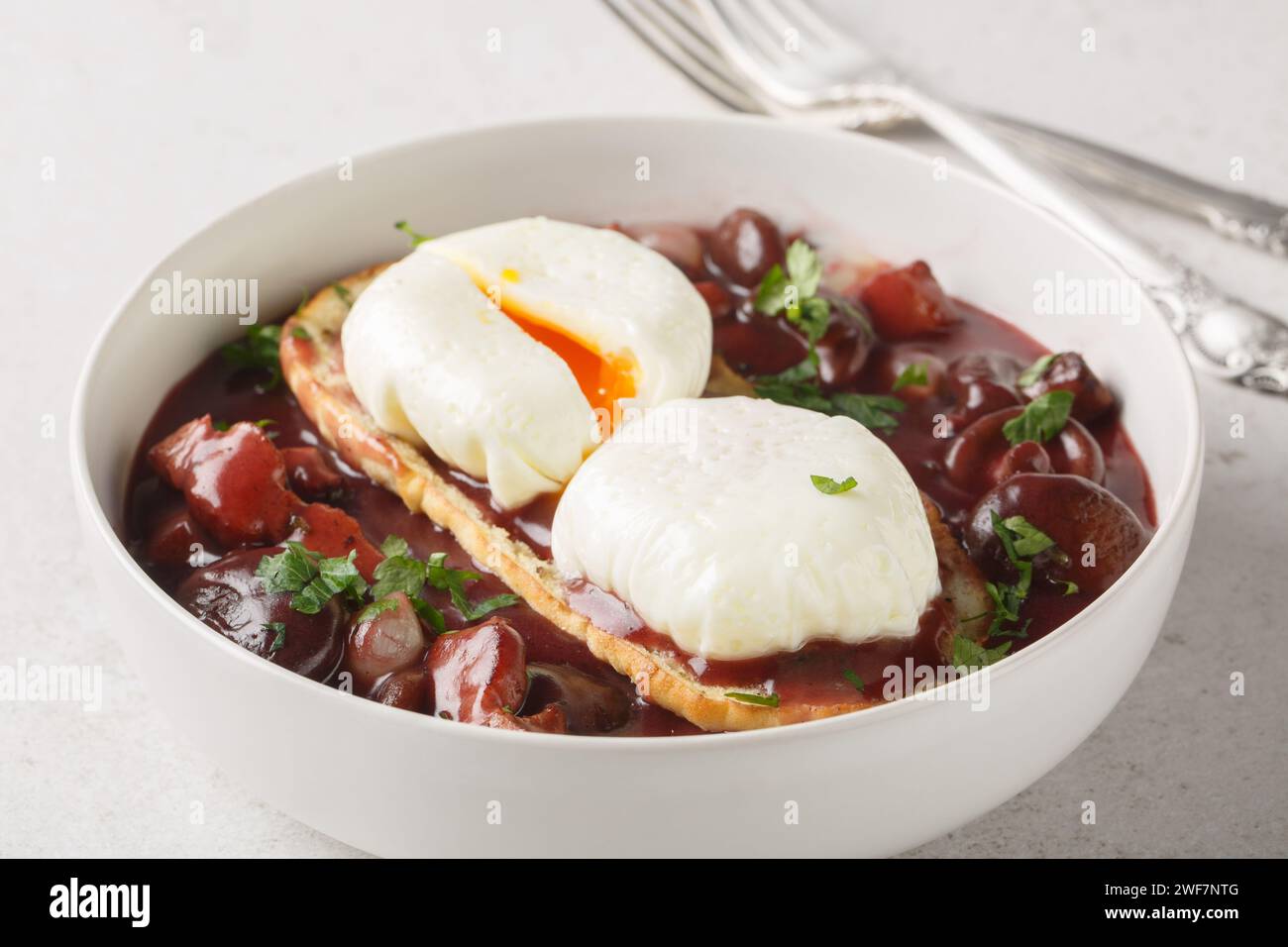 Oeufs en meurette è un classico piatto francese di uova in camicia ricoperto da una ricca salsa di vino rosso ripiena di lardoni, funghi e cipolla primo piano sul PL Foto Stock