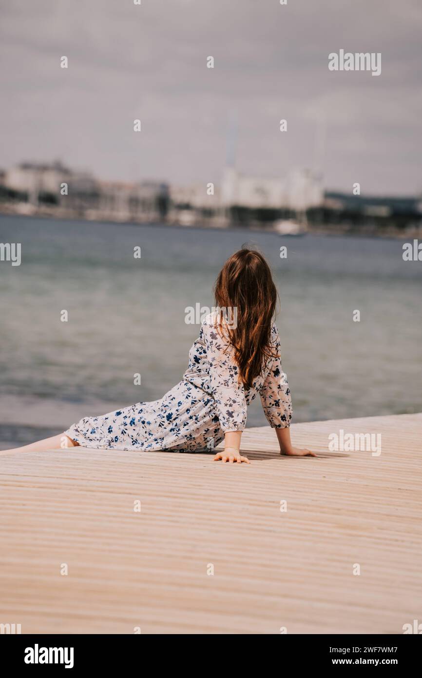 Serenità estiva: La donna in abito estivo gode della vista sul mare sul molo di fronte allo skyline della città Foto Stock