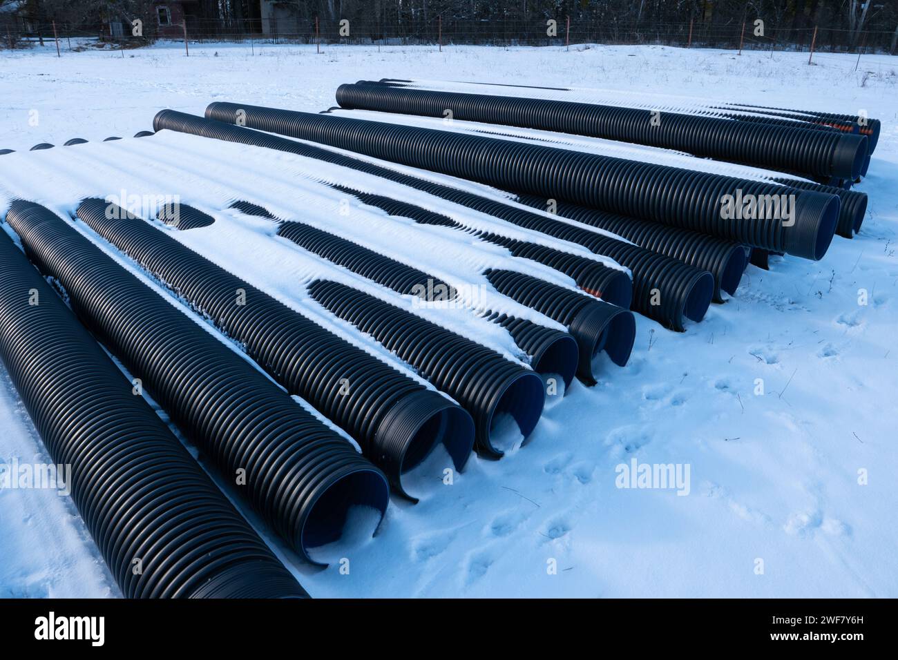 I tubi di drenaggio corrugati in plastica nera sono disposti in modo ordinato sulla superficie innevata durante l'inverno. Foto Stock