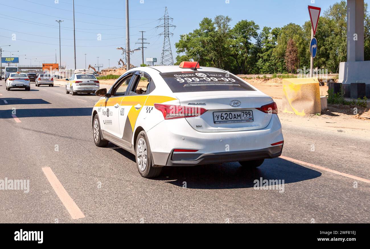 Mosca, Russia - 6 luglio 2021: Il taxi Yandex scende per strada nel pomeriggio. Il taxi bianco Hyundai Solaris scende in fondo alla strada. Moderno taxi cittadino Foto Stock