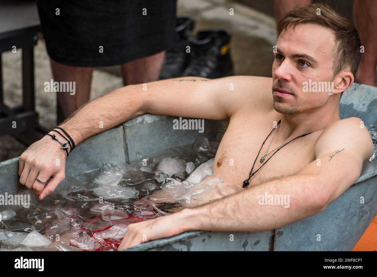 Bel ragazzo che fa il bagno nell'acqua fredda tra cubetti di ghiaccio in una vasca d'epoca. Metodo Wim Hof, terapia fredda, tecniche respiratorie, meditazione Foto Stock