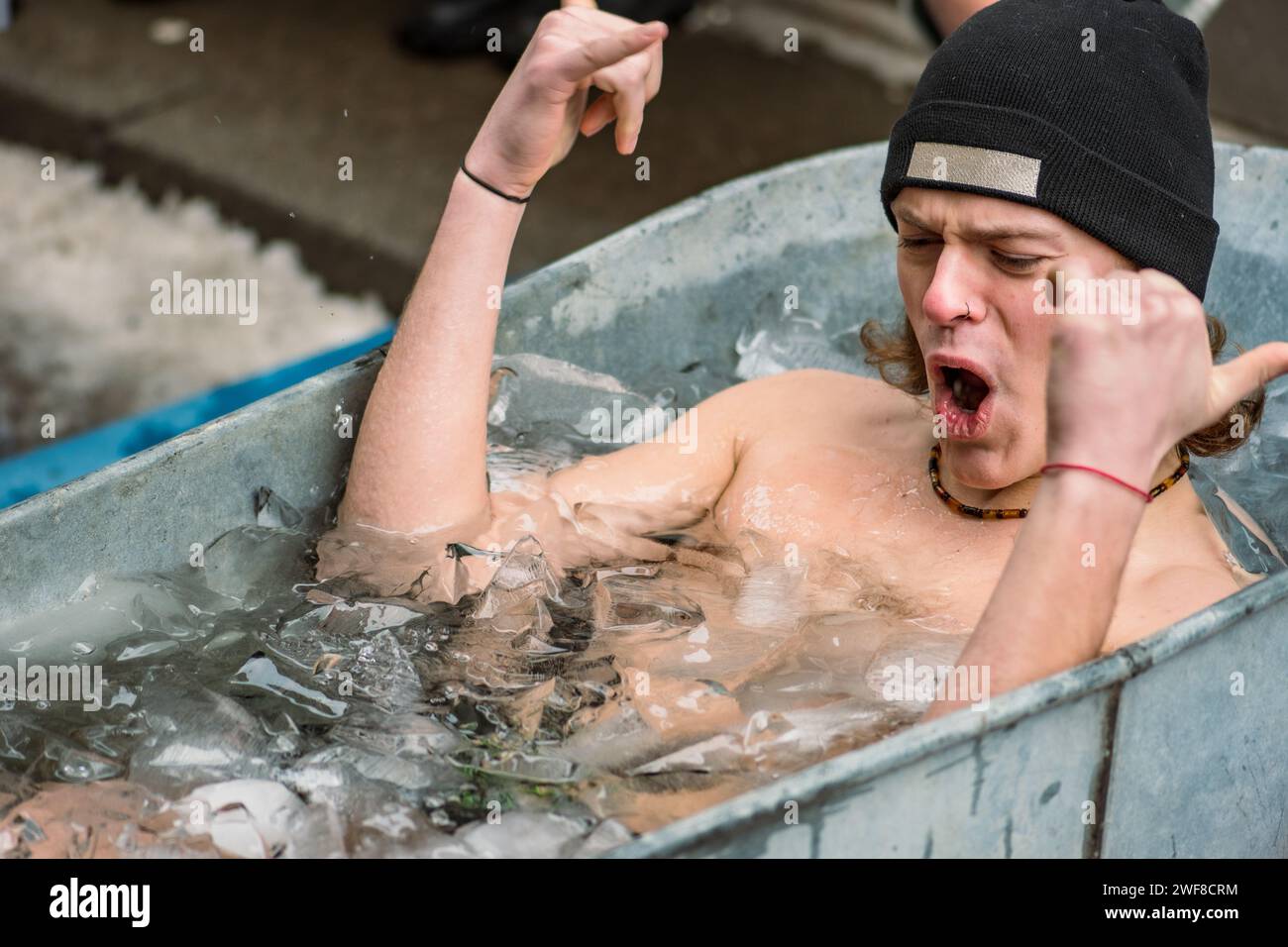 Bel ragazzo che fa il bagno nell'acqua fredda tra cubetti di ghiaccio in una vasca d'epoca. Metodo Wim Hof, terapia fredda, tecniche respiratorie, meditazione Foto Stock