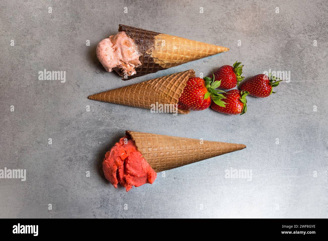 Coni per gelato con misurini di gelato alla fragola e fragole di frutta. Messa a fuoco morbida Foto Stock