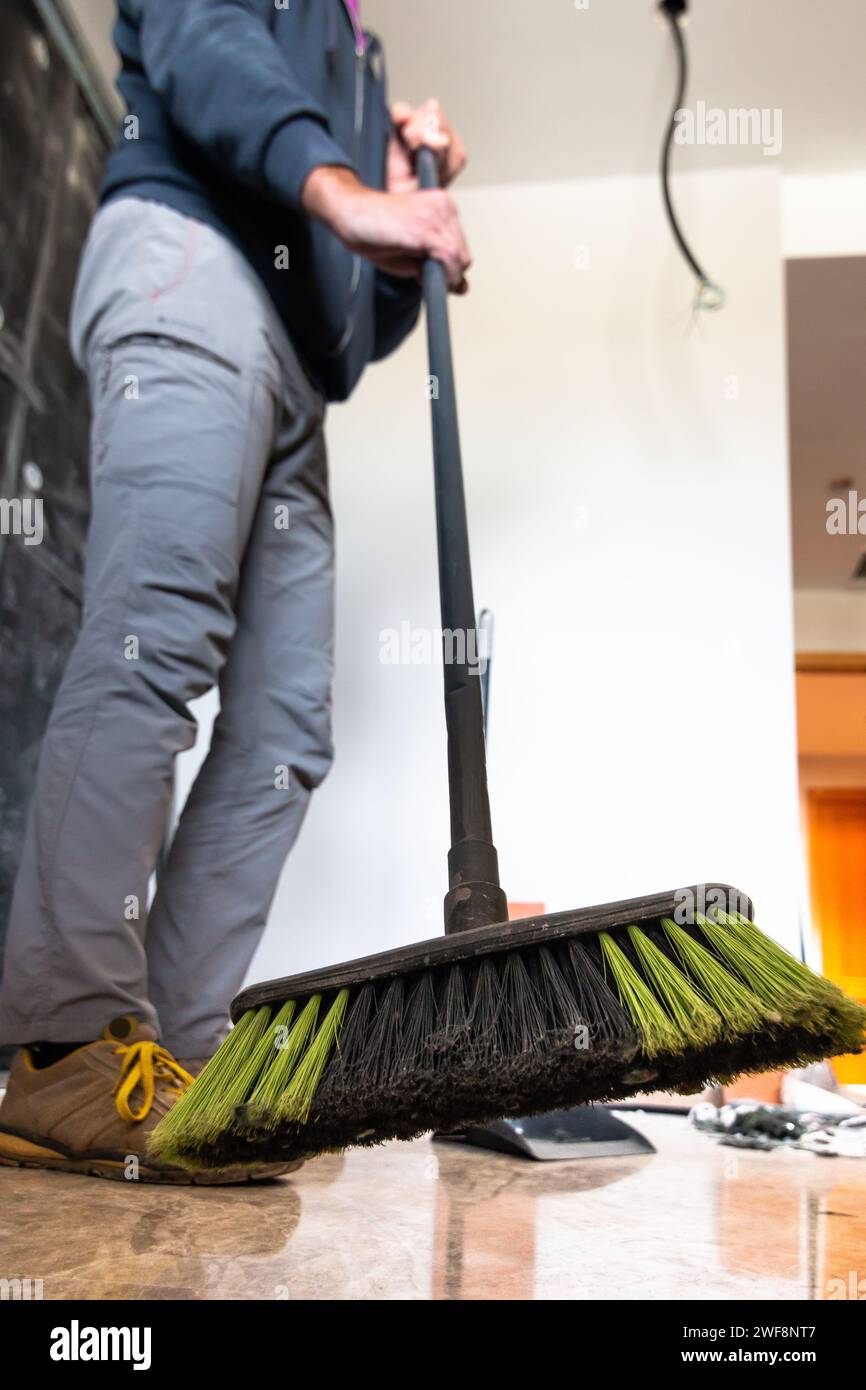 L'immagine ad angolo ridotto di uno strato di mattoni con una scopa spazza il pavimento in un cantiere edile. Messa a fuoco selettiva con la scopa in primo piano. Ristrutturazione della casa Foto Stock