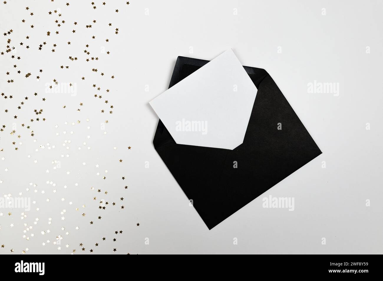 Composizione natalizia, busta nera, coriandoli con stelle dorate su sfondo bianco. Natale, Capodanno, inverno. Vista dall'alto, base piatta, spazio di copia. Foto Stock