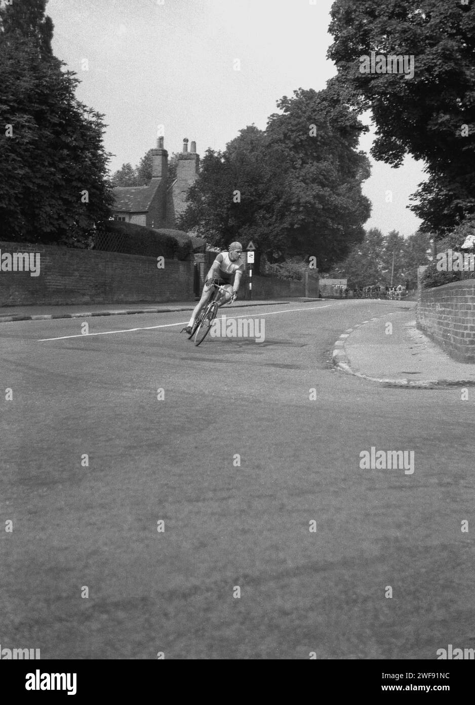 1964, storico, sport ciclistico, un pilota maschile su una strada che affronta una curva nella corsa ciclistica Tour of Britain, con il pacchetto di ciclisti da corsa visti sullo sfondo, Inghilterra, Regno Unito. Foto Stock