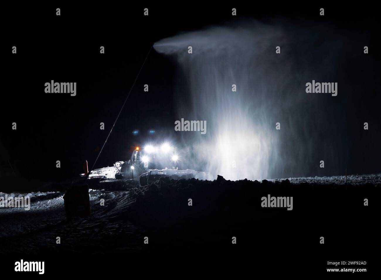 Un rastrello che opera di notte sotto un cannone innevato in Val-Cenis, una stazione sciistica delle Alpi francesi Foto Stock