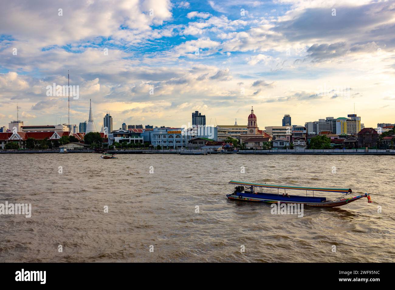Una barca galleggia pacificamente sul fiume accanto a una vivace città, creando un contrasto sorprendente tra la natura e la vita urbana. Foto Stock