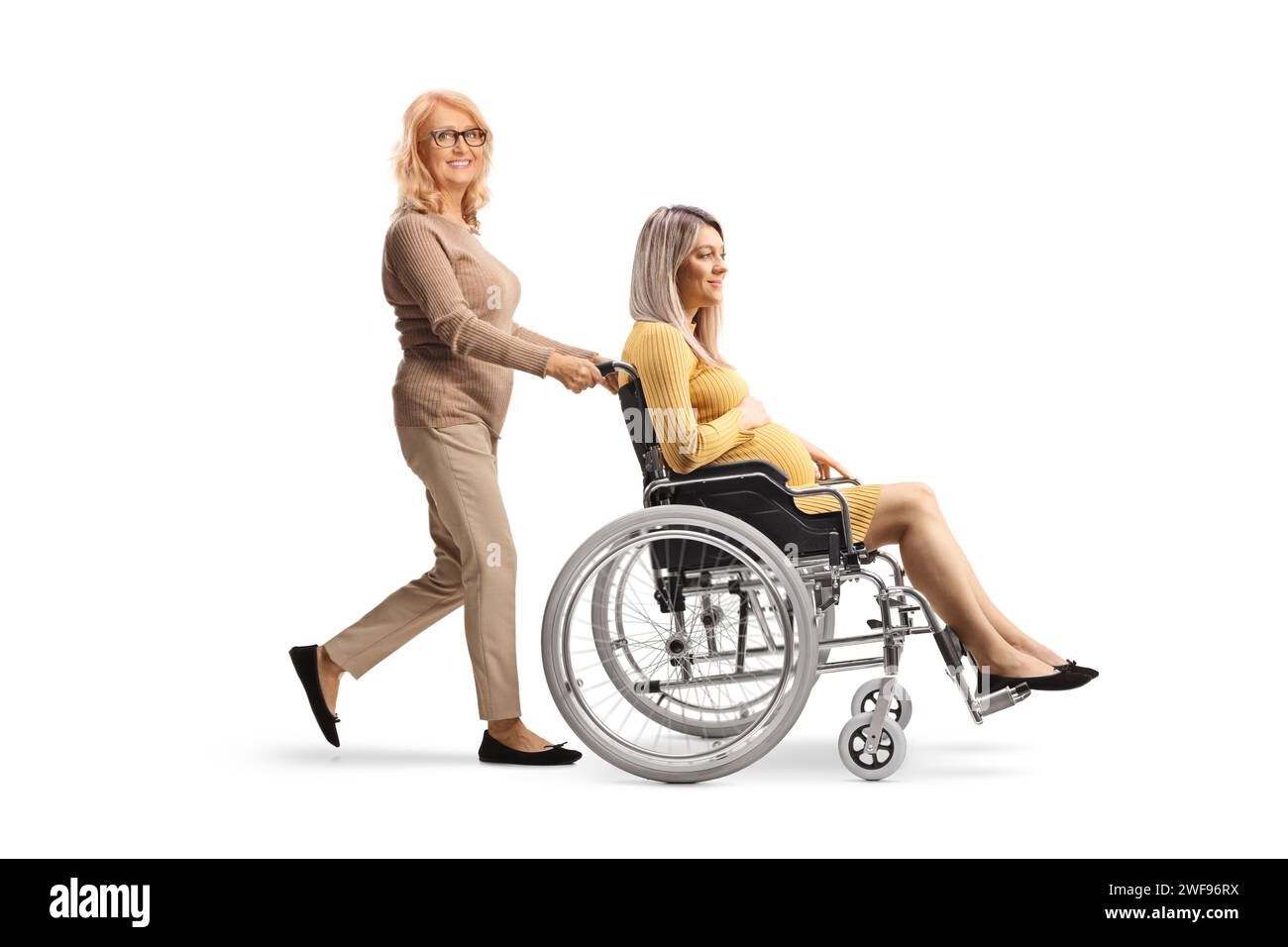Donna di mezza età che spinge una donna incinta su una sedia a rotelle isolata su sfondo bianco Foto Stock