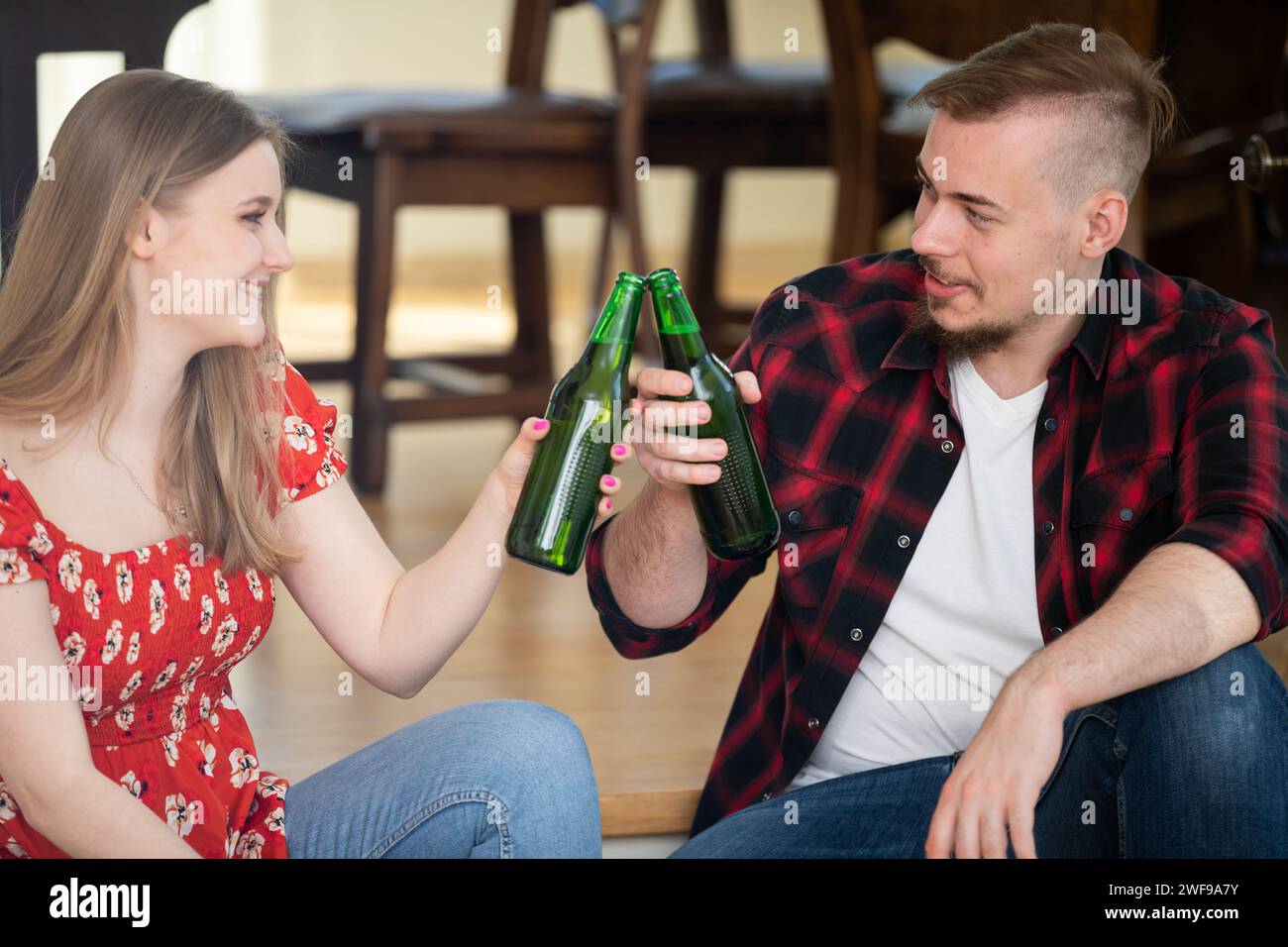 Un uomo e una donna siedono a casa e brindano con delle bottiglie di birra. Foto Stock