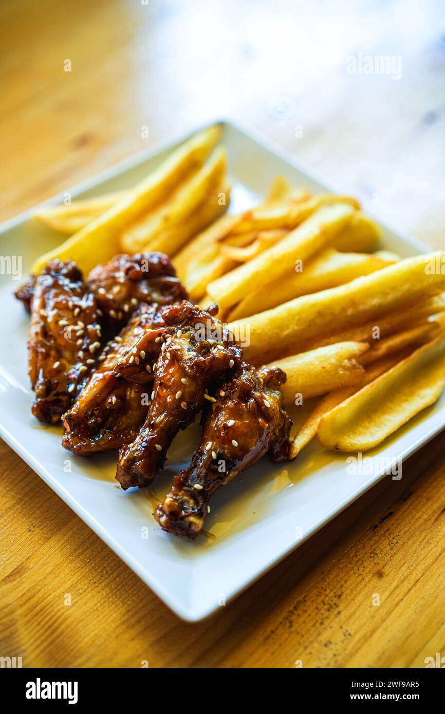 Ali di pollo al forno e cosce con patatine fritte su un piatto. Foto Stock