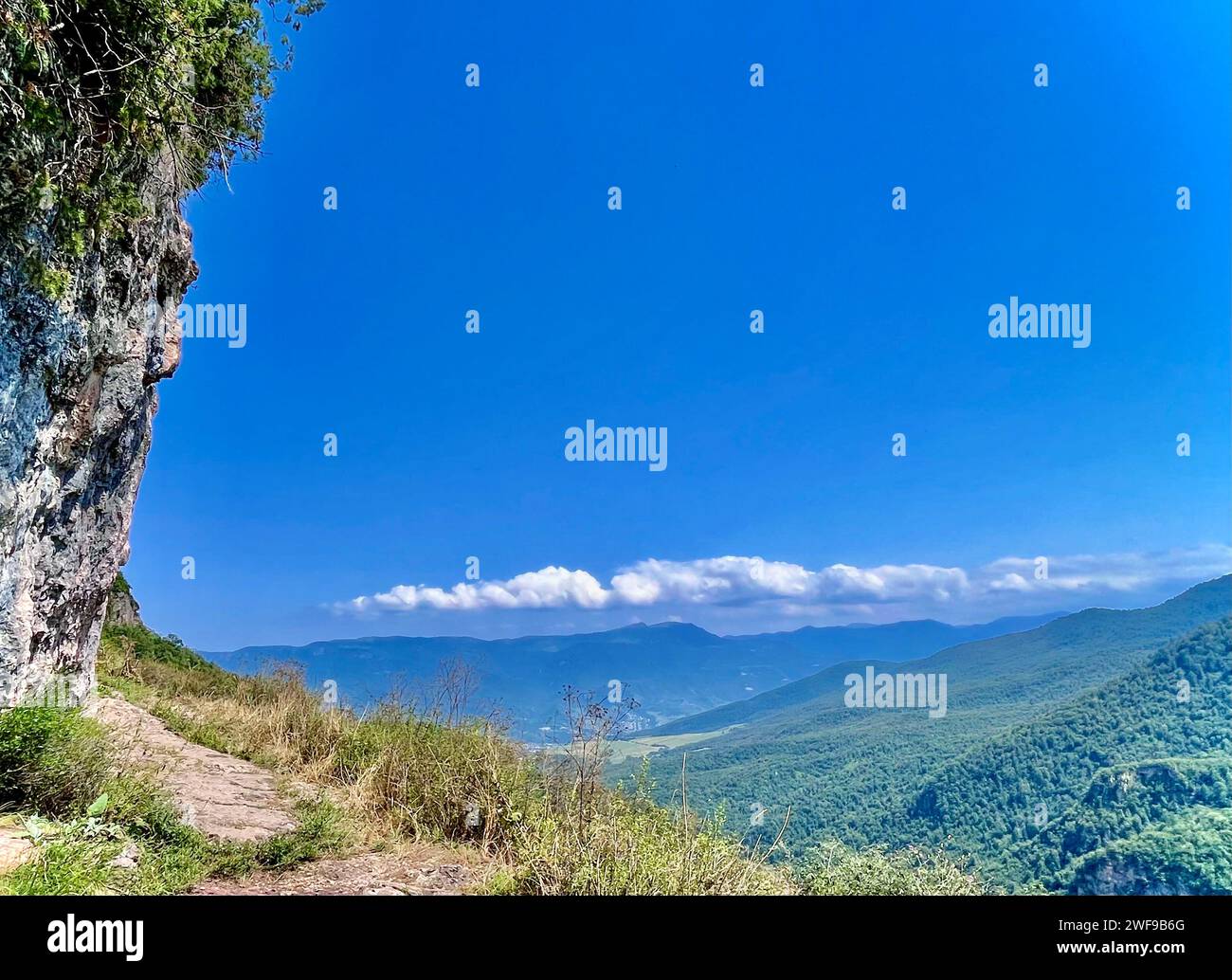 Cima rocciosa con sentieri e alberi, incorniciata da un cielo azzurro Foto Stock