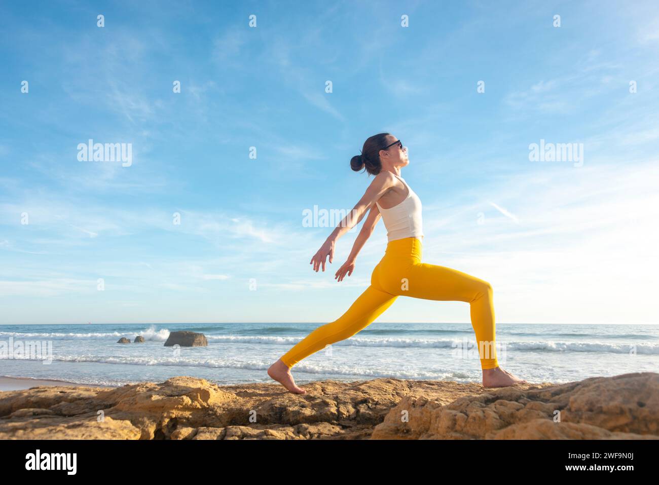 donna che fa pilates esercizi di stretching in spiaggia su una roccia Foto Stock