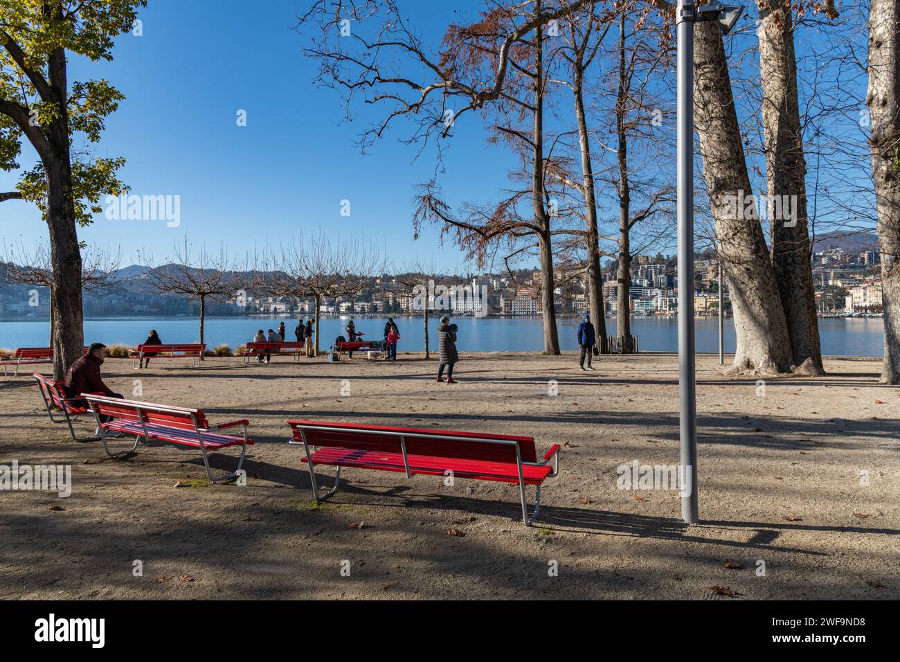La gente sedeva sulle panchine in un parco sul lago di Lugano in Svizzera Foto Stock