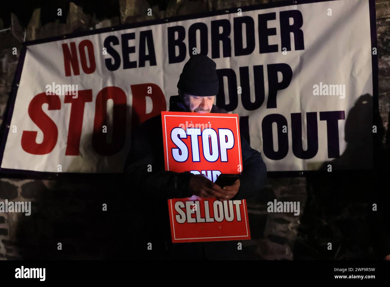Un manifestante controlla il suo telefono cellulare mentre si trova fuori Larchfield Estate, dove il DUP sta tenendo una riunione privata, chiedono al DUP di non tornare a Stormont fino a quando il confine con il Mare d'Irlanda non sarà rimosso. Data immagine: Lunedì 29 gennaio 2024. Foto Stock