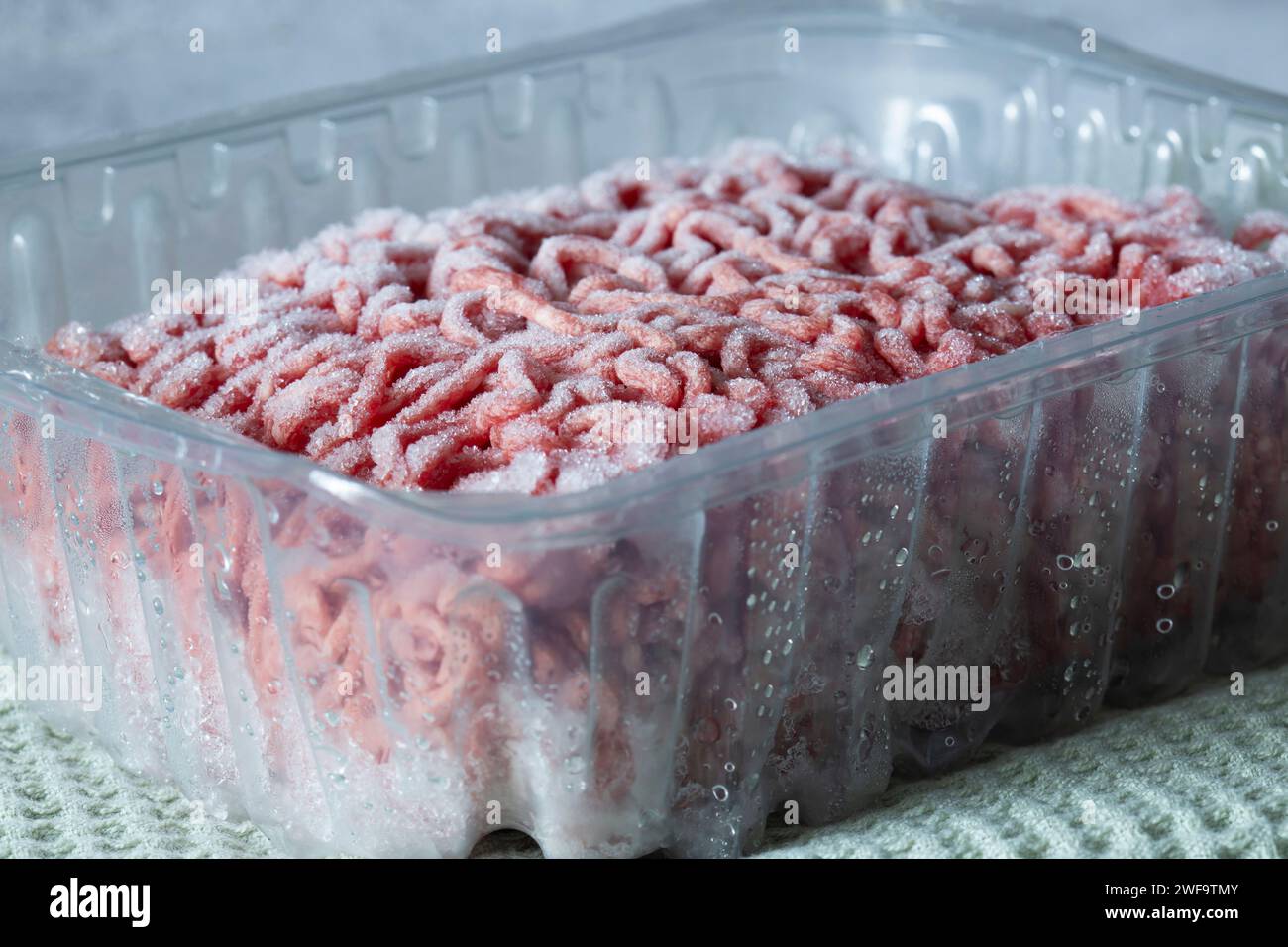 Tritare la bistecca di manzo congelata in un contenitore di plastica scongelando. Su un telo da tè verde. Foto Stock