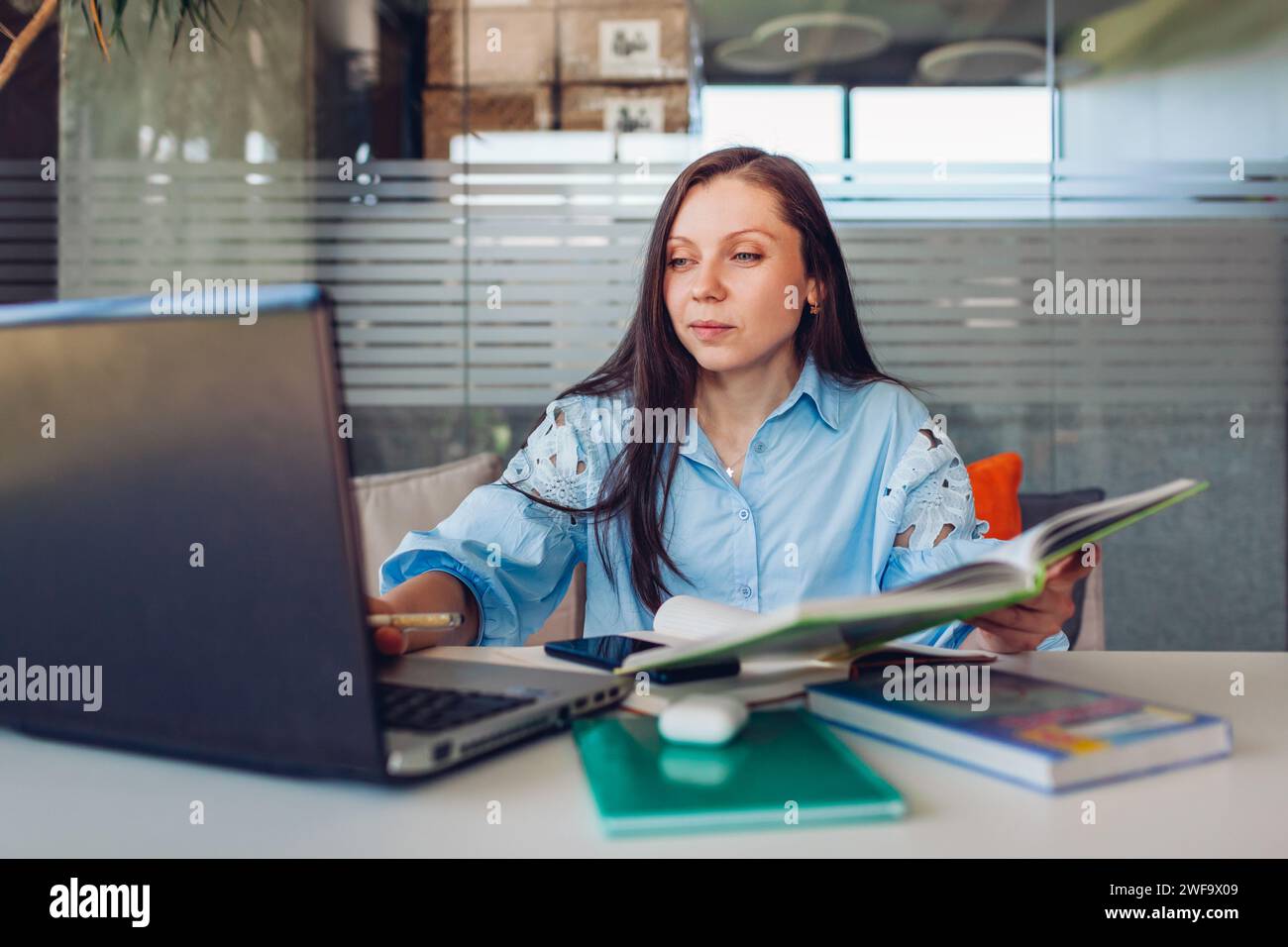 Giovane donna d'affari che lavora online in ufficio utilizzando un computer portatile. Insegnante donna di mezza età alla ricerca di informazioni seduto alla scrivania. Foto Stock