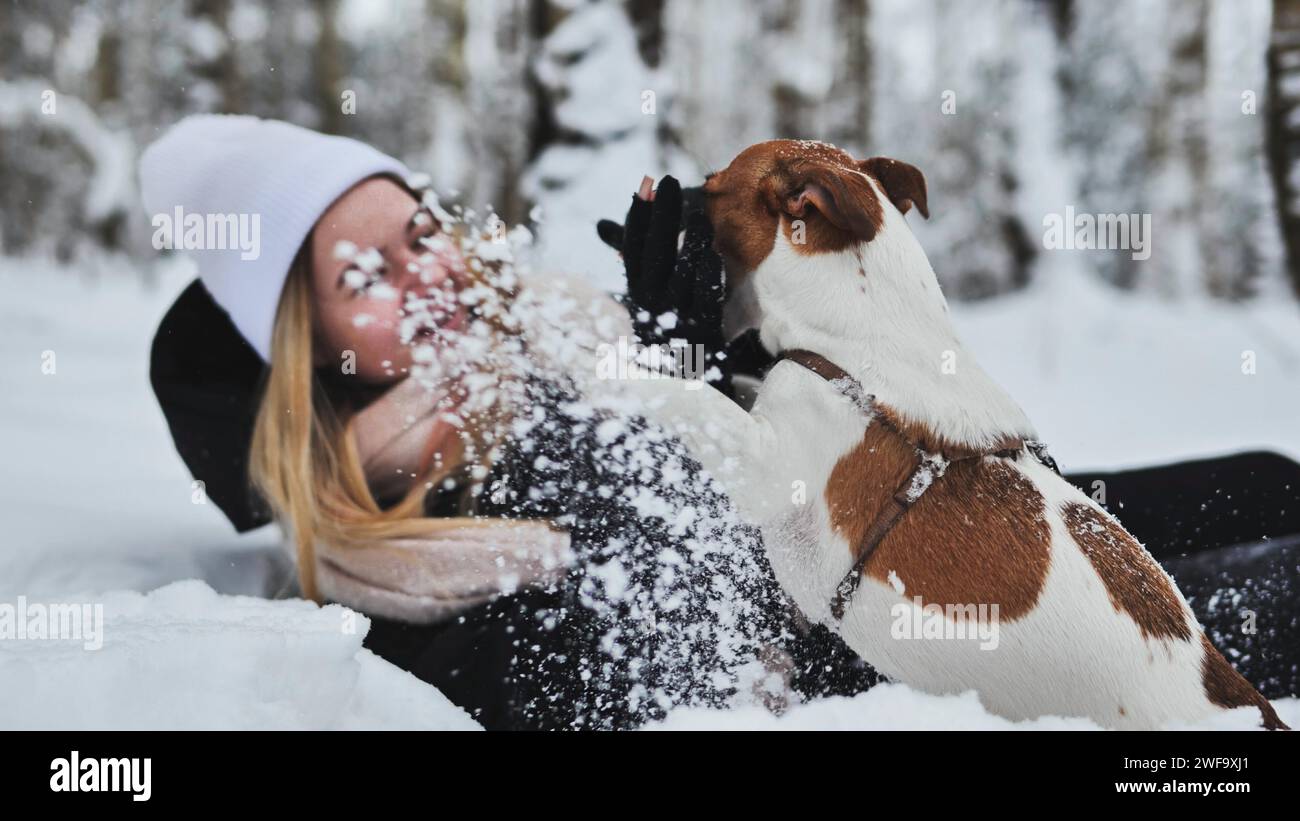 Una ragazza cade nella neve con il suo cane Jack Russell Terrier in inverno. Foto Stock