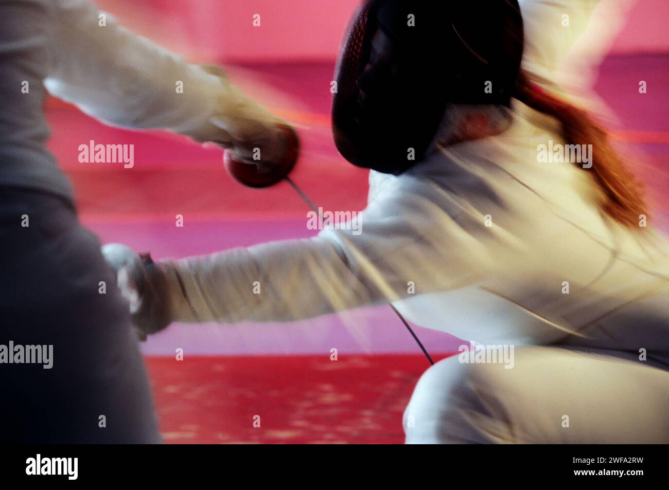 Due schermidori si impegnano in un duello frenetico, con un atleta che esegue un affondo contro il proprio avversario durante un torneo di scherma. Foto Stock