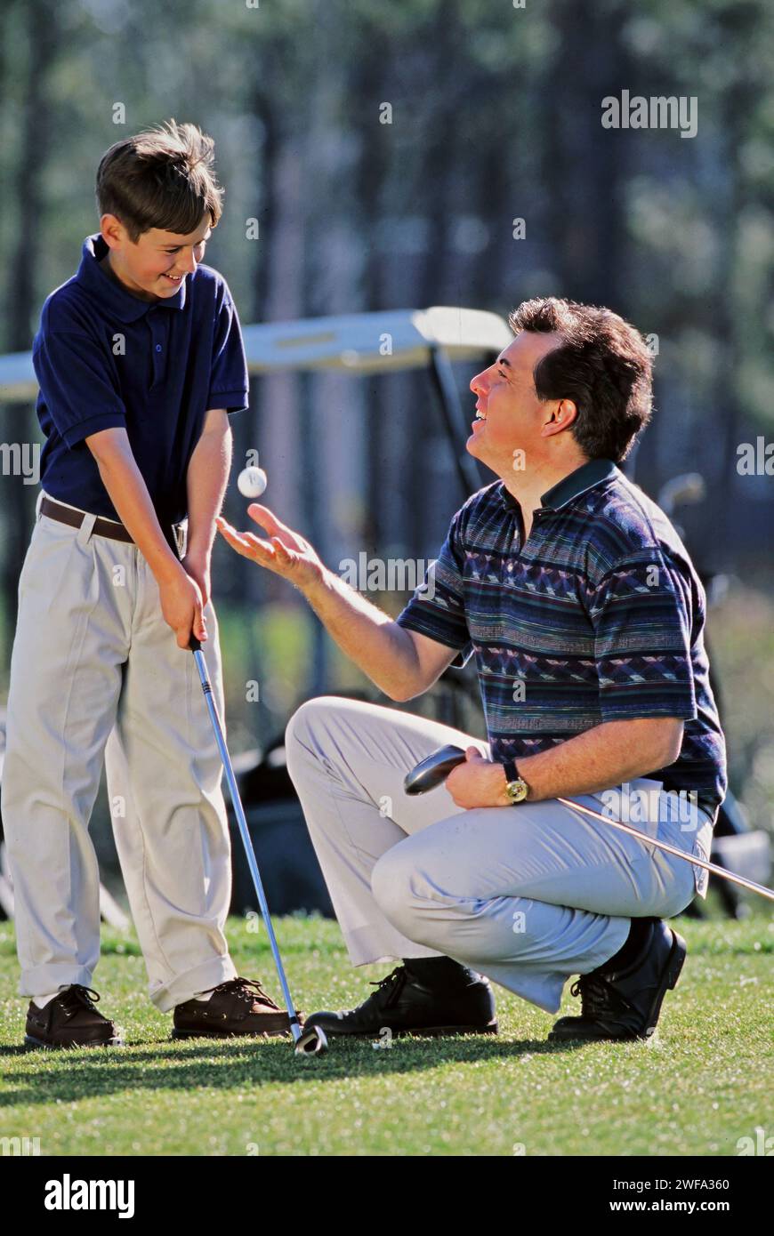 Un padre sta dando una lezione di golf a suo figlio su un campo verde lussureggiante in una giornata luminosa e soleggiata. Foto Stock