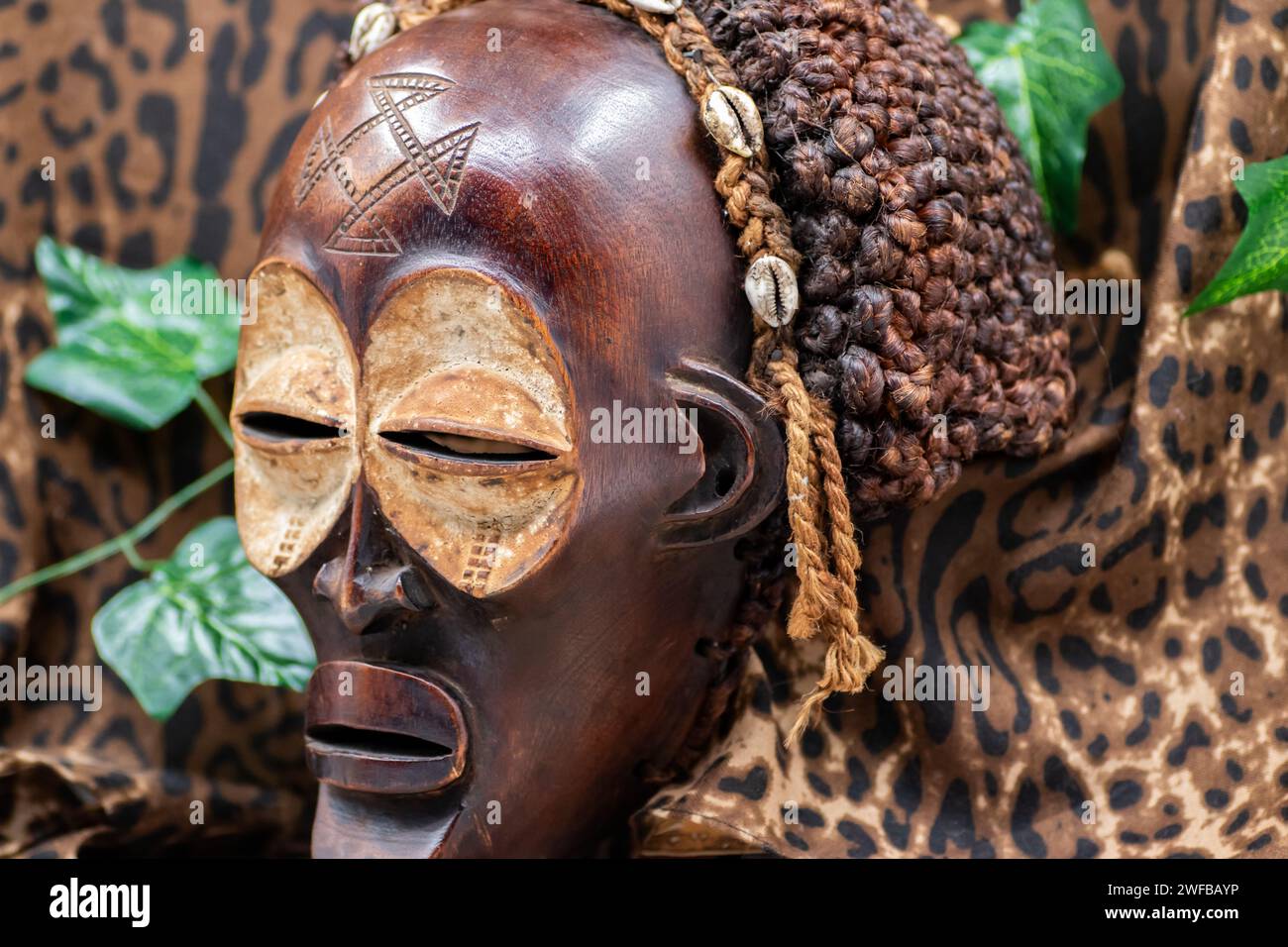 Maschera africana tribale in legno dall'Uganda, per la famiglia o la protezione personale, realizzata in legno locale, corde e conchiglie come decorazione dei capelli Foto Stock