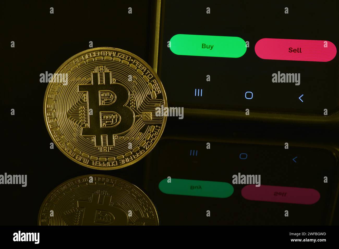 Fotografia di Bitcoin dorato su una superficie nera riflettente, compresi i pulsanti di acquisto e vendita sul telefono cellulare per investimenti o trading. Foto Stock