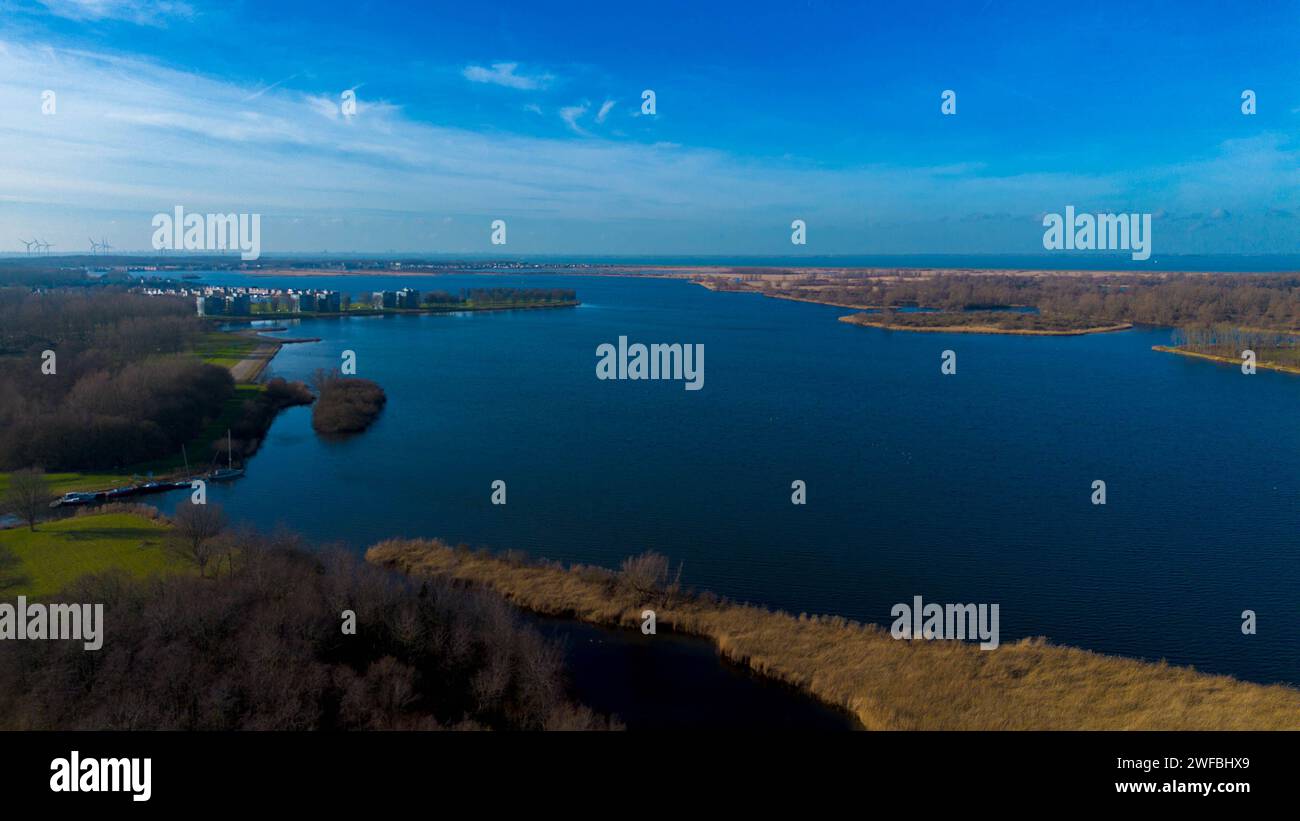 Una vista panoramica del lago con vegetazione lussureggiante, edifici distanti e dintorni sereni Foto Stock