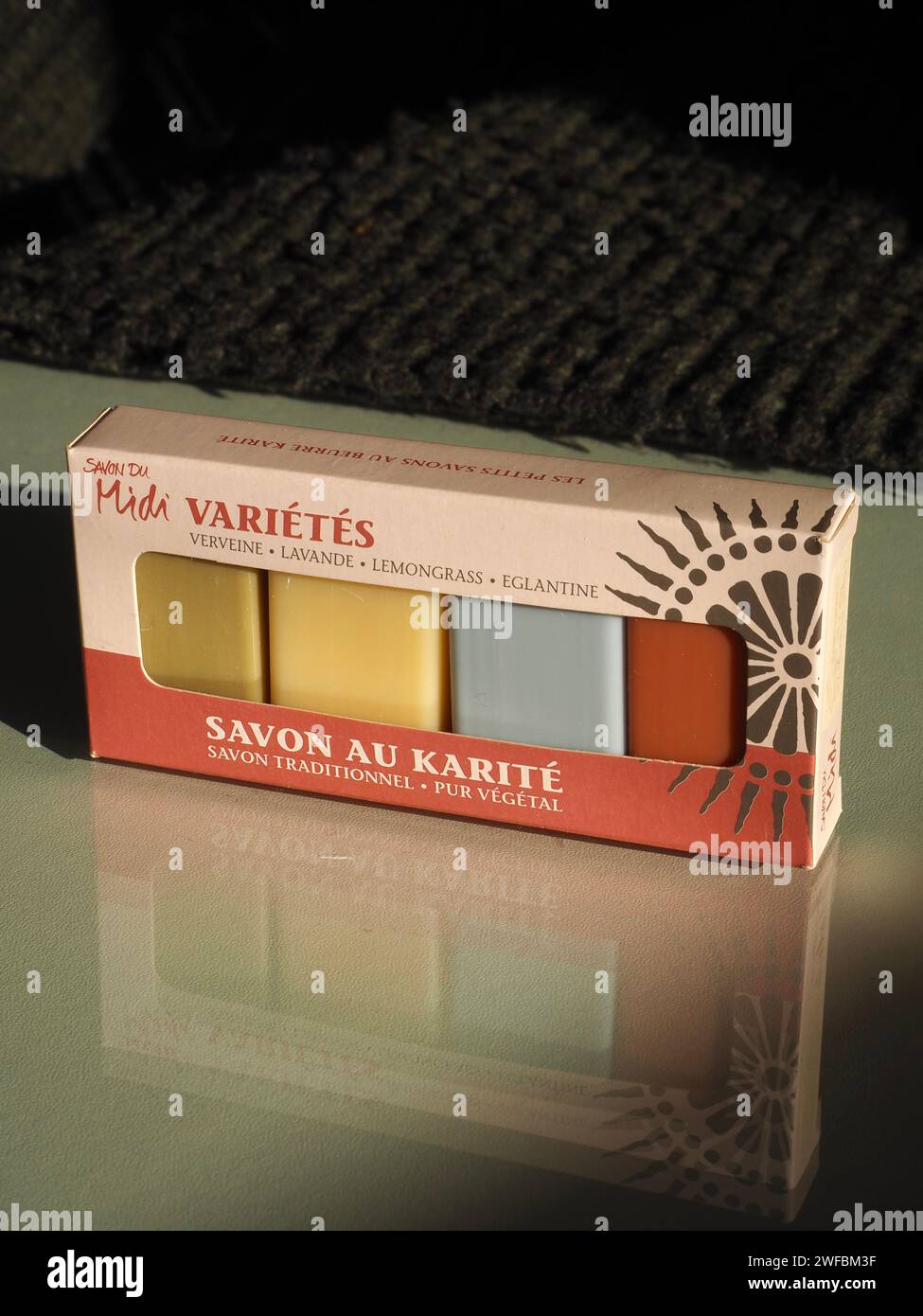 Confezione variegata di 4 saponi ospiti con profumi di verbena, lavanda, citronella e rosa selvatica. “Savon au karité”, sapone burro di karité. Immagine riflessa nel vetro. Foto Stock