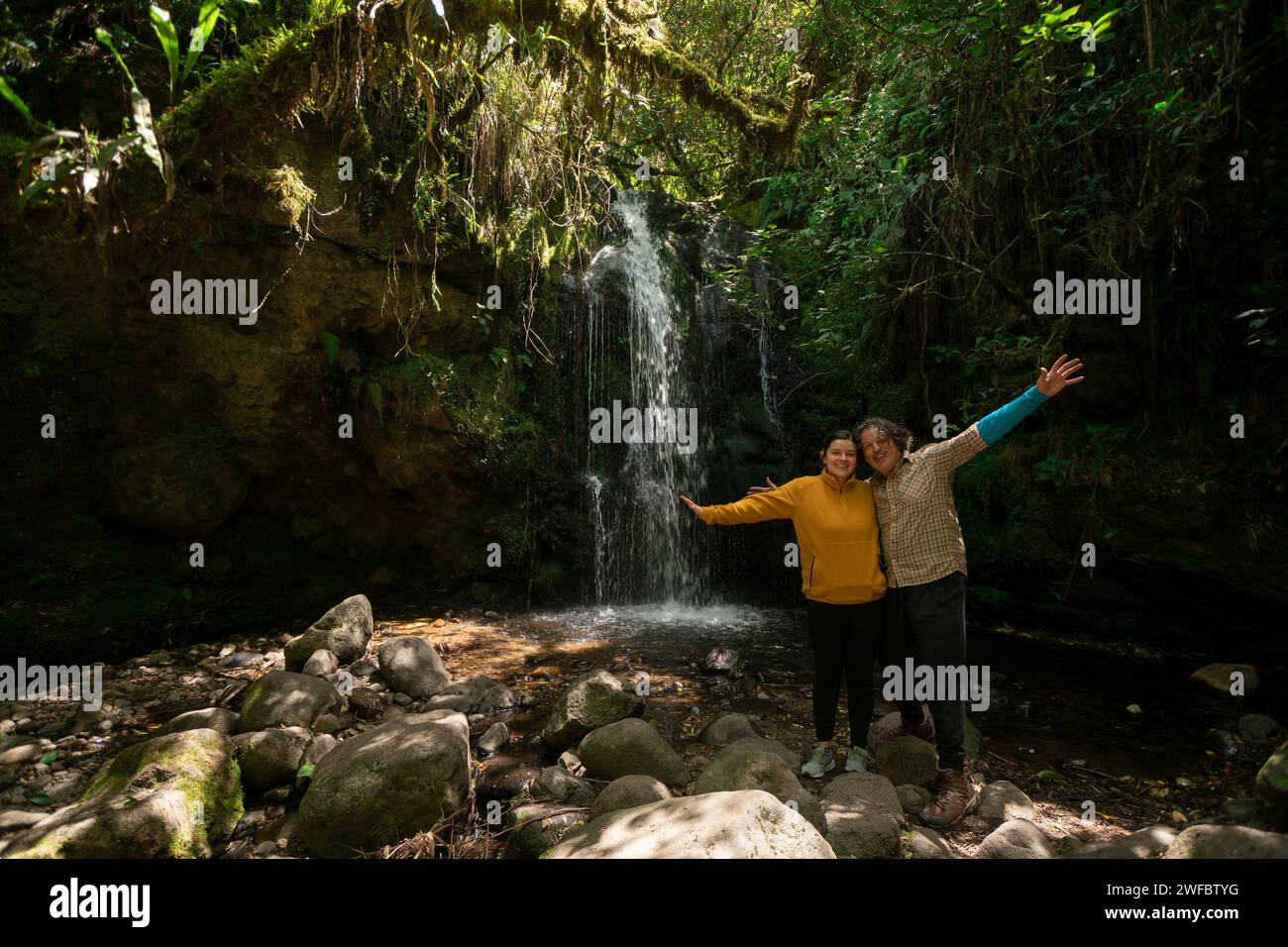 Ritratto di una giovane coppia che scatta foto accanto a una cascata nel mezzo di una foresta durante una giornata di sole Foto Stock