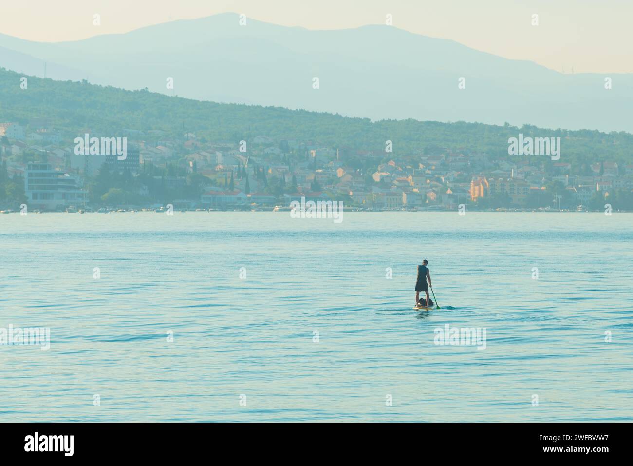 Persona irriconoscibile stand-up paddle boarding nel mare Adriatico Golfo del Quarnero visto dalla costa della città di Crikvenica, attenzione selettiva Foto Stock