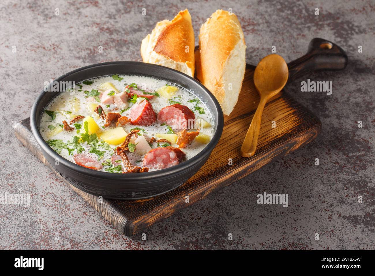 Zuppa di patate e pasta madre di segale tradizionale Zalewajka con salsiccia e funghi secchi, primo piano sul piatto sul tavolo. Orizzontale Foto Stock