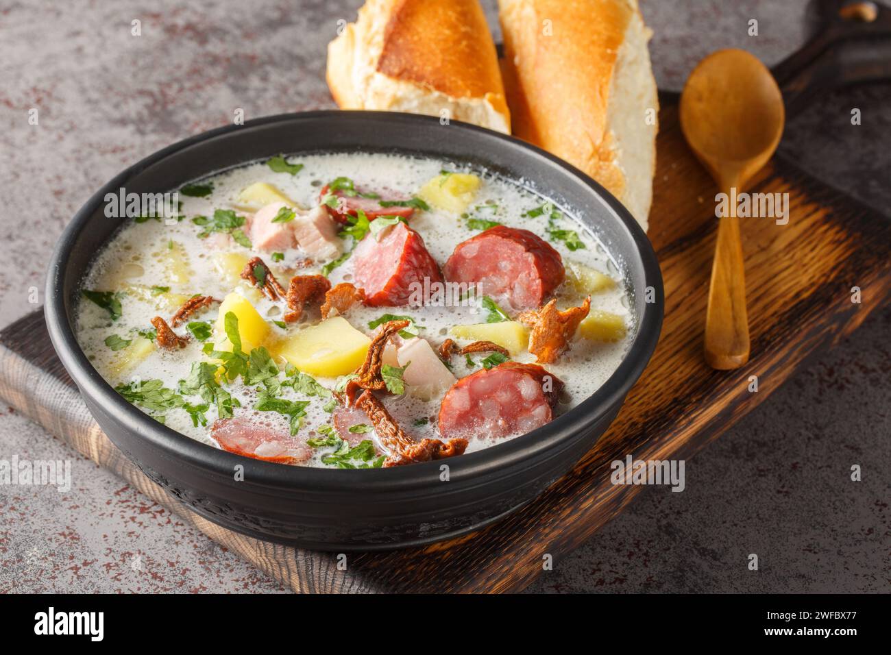 Zalewajka è una deliziosa zuppa di segale acida polacca tradizionale con verdure, salsiccia e funghi secchi da vicino sul piatto sul tavolo. Orizzontale Foto Stock