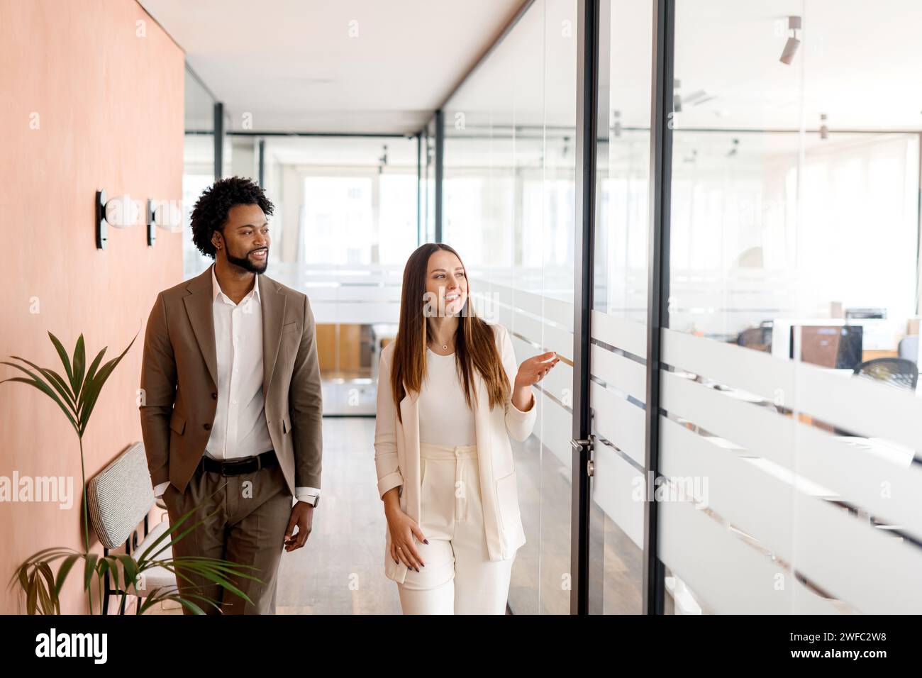 Un uomo d'affari afro-americano e la sua collega donna condividono una visione strategica che attraversa l'ufficio, con sorrisi genuini che indicano una cultura del lavoro positiva. Concetto di collaborazione e lavoro di squadra Foto Stock