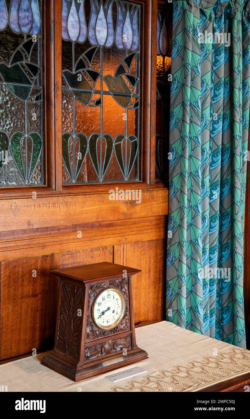 Regno Unito, Cumbria, Bowness on Windermere, Blackwell, Arts and Crafts House, Main Hall, orologio in rovere intagliato dalla finestra interna in vetro piombato Foto Stock