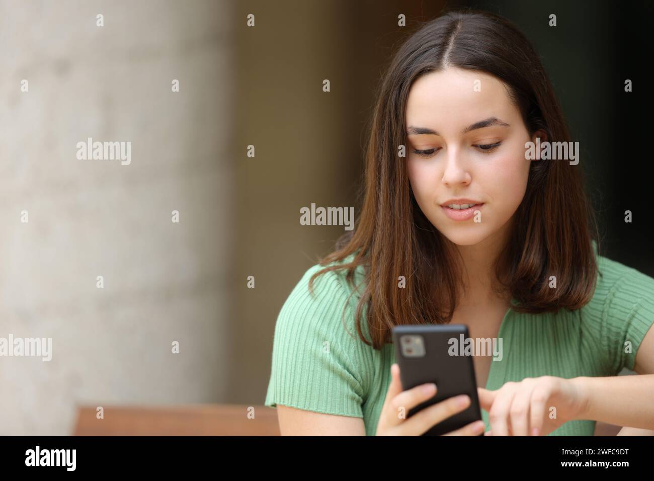 Vista frontale di una donna che controlla uno smartphone su una panchina Foto Stock