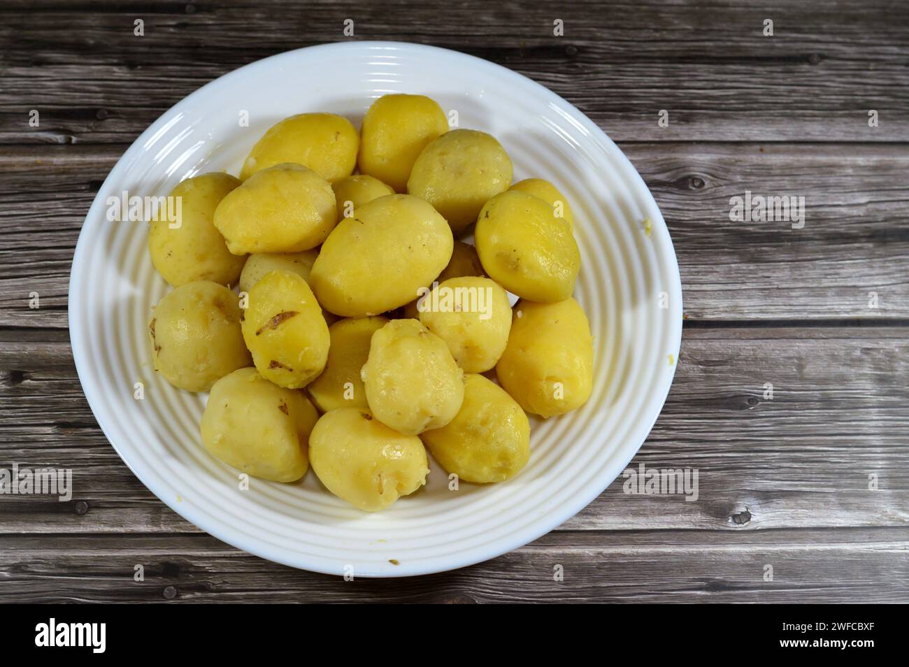 palline di patate bollite in acqua calda, da friggere poi in olio per alimenti profondi, fast food di patate come contorno o spuntino, serviti in un piatto su un babbo di legno Foto Stock