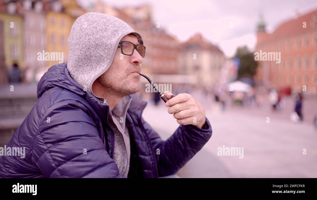 Ritratto di un uomo adulto con occhiali seduti nel cappuccio sulla piazza e fumare un tubo di tabacco nella Piazza del Palazzo, nella Città Vecchia di Varsavia Foto Stock