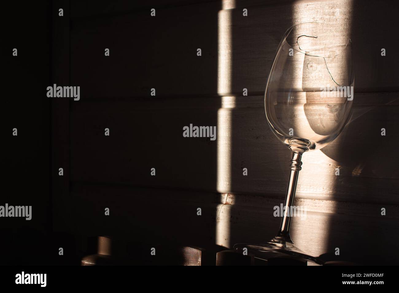 vetro rotto alla luce del sole su fondo di legno. Bicchiere da vino danneggiato con bordi affilati. Vetro incrinato nelle ombre. Natura morta creativa. Oggetto fragile Foto Stock