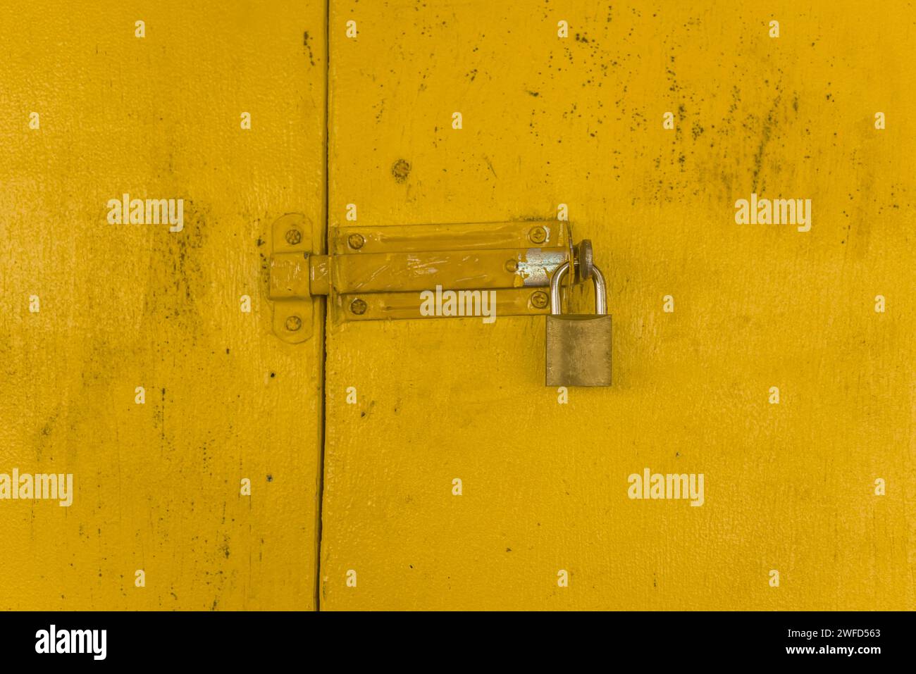 Lucchetto su cancello di legno giallo che forma uno sfondo ruvido. Foto Stock