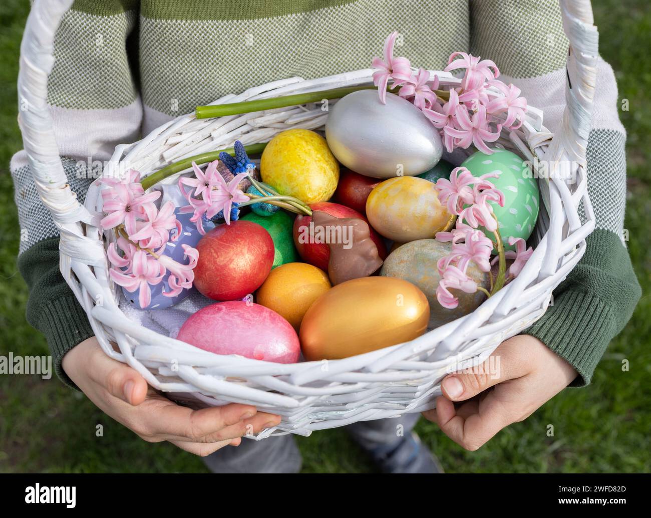 Bellissime uova di Pasqua colorate e fiori di Giacinto in un cestino di vimini bianco nelle mani di un bambino. Tradizioni di famiglia. Pasqua divertente, bambino interessante Foto Stock