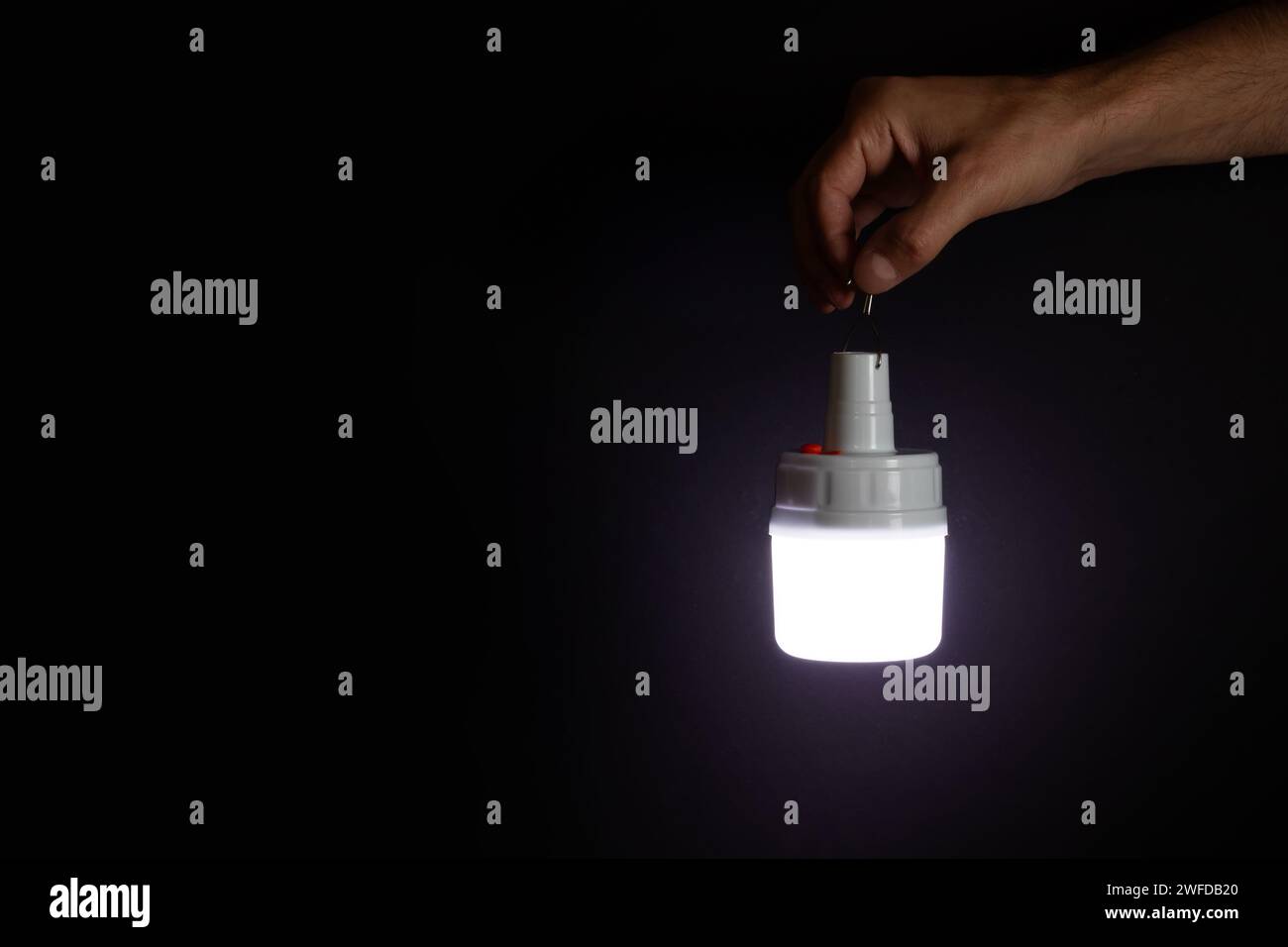 La mano di un uomo contiene una luce di emergenza a LED ricaricabile portatile con batteria integrata e illumina la salita delle scale. Fonte di luce durante la bla Foto Stock