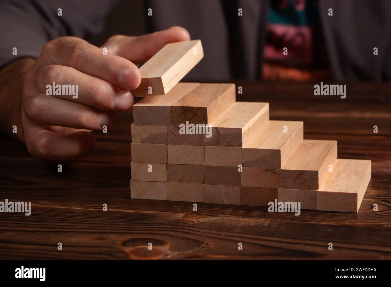 un uomo d'affari costruisce un gioco di blocchi di legno. Foto Stock