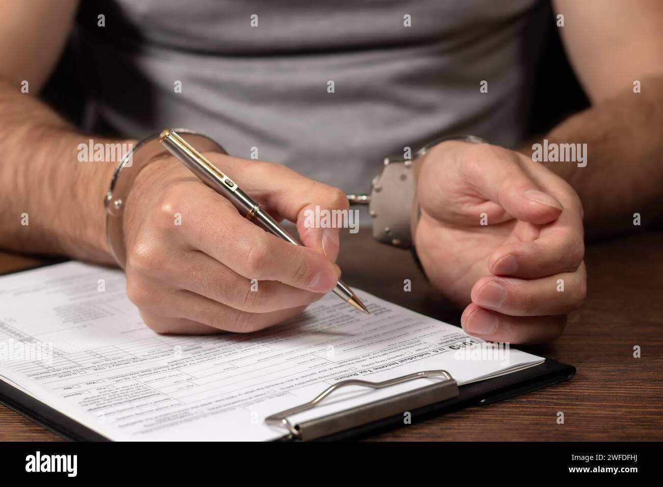 Evasione fiscale, criminalità e frode. Uomo in manette che compila il modulo delle imposte documenti di dichiarazione dei redditi e manette Foto Stock