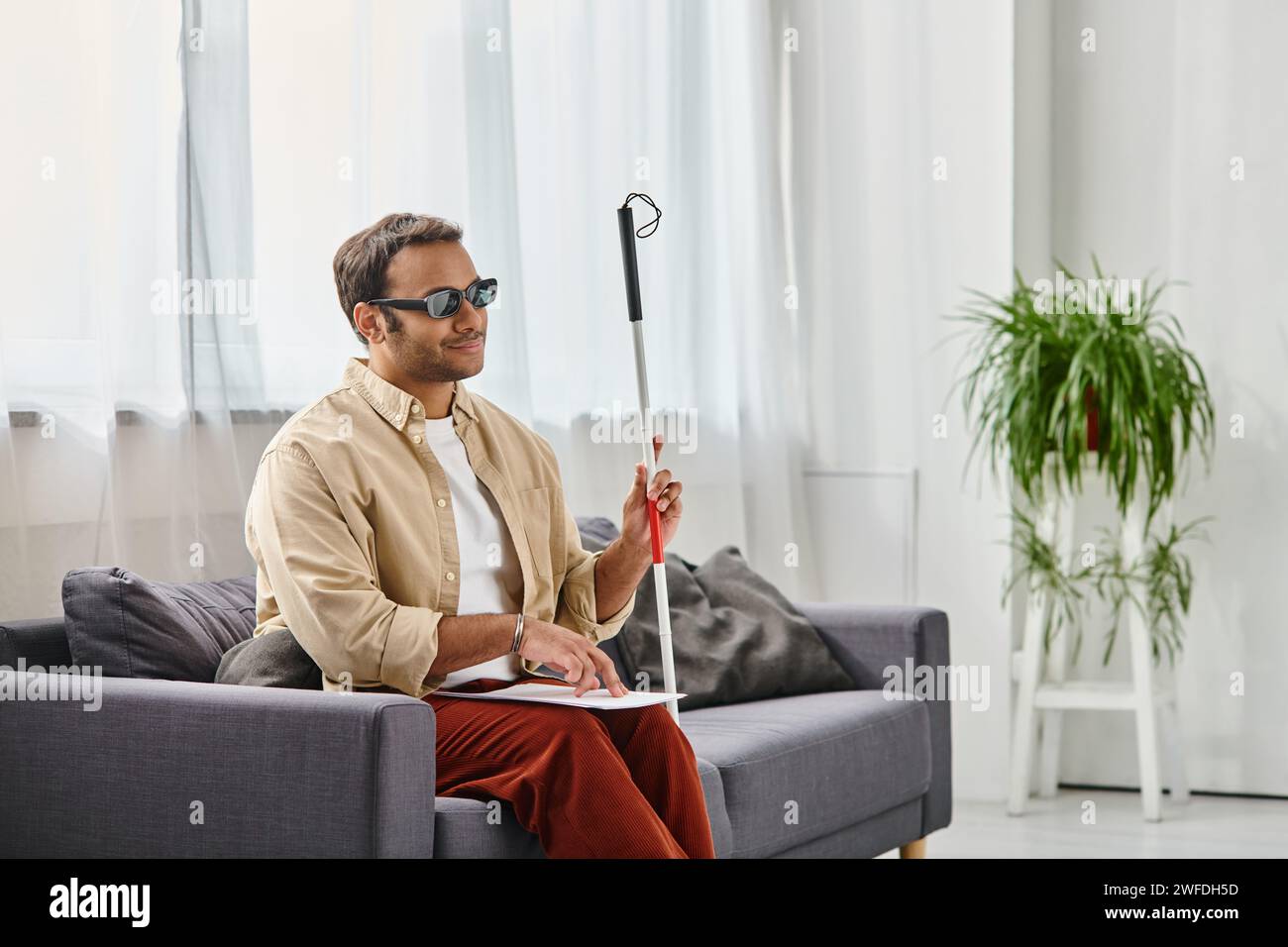 gioioso indiano con disabilità visiva con occhiali e bastone da passeggio che legge il codice braille Foto Stock