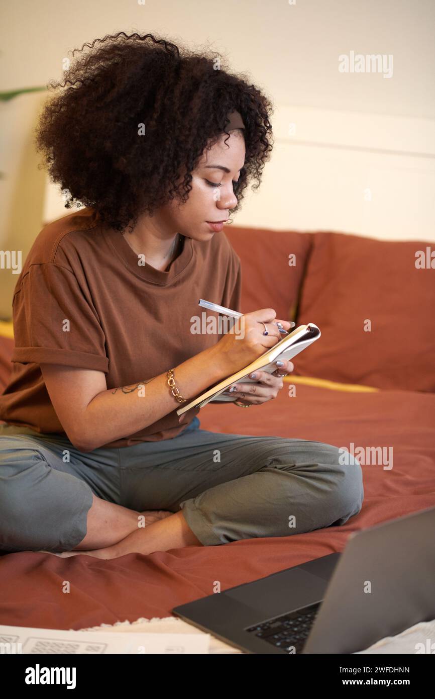 Donna seduto a letto, guardando video educativi e prendendo appunti in planner Foto Stock