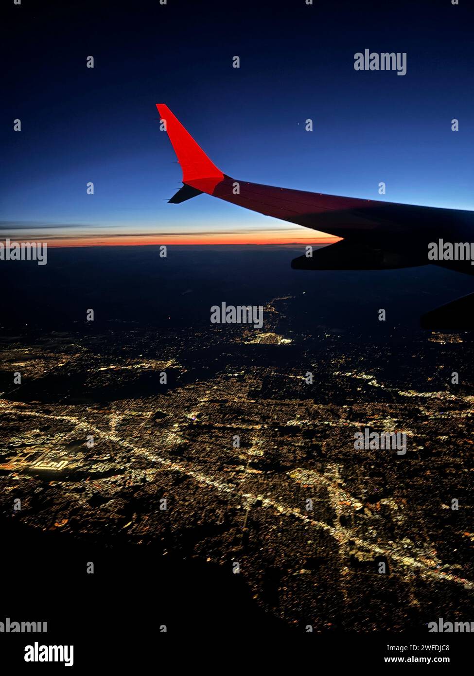 Aereo che vola da solo sopra il paesaggio urbano illuminato al crepuscolo Foto Stock