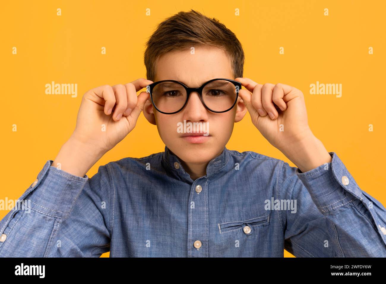 Ragazzo adolescente concentrato con camicia in denim che regola i suoi grandi occhiali neri Foto Stock