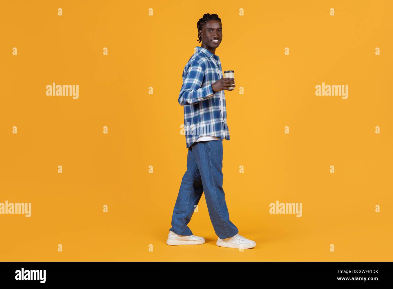 Giovane uomo nero rilassato che cammina con una tazza di caffè da asporto in mano Foto Stock