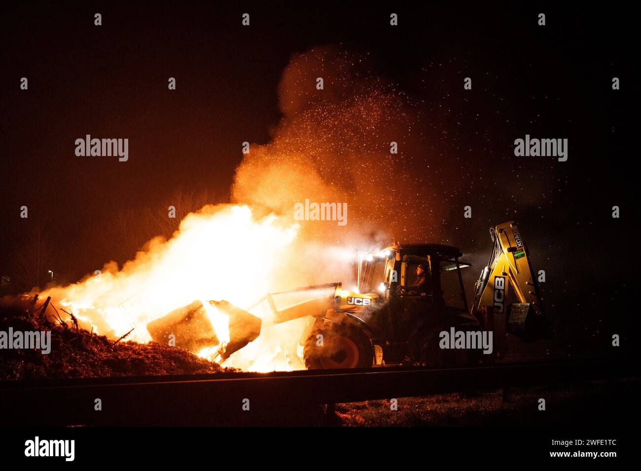 © PHOTOPQR/OUEST FRANCE/GUILLAUME SALIGOT/OUEST-FRANCE ; Ploudaniel ; 29/01/2024 ; blocage de la N12 par les Agriculture notamment de la FNSEA/FDSEA et des Jeunes Agriculteurs du Finistere 29 . Au niveau de l'echangeur de Mescoden à Ploudaniel (Finistere). De nombreux tracteurs etaient Presents, des feux ont ete allumes et les Agriculture ont prevu de passer la nuit sur Place . Crise agricole . Colere des Agricoltura . Agriculteurs en colere . ICI un agricolteur use un engin de chantier pour degager la Route alors que d' autres manifestants ont mis le feu a un tas de dechets sur Foto Stock