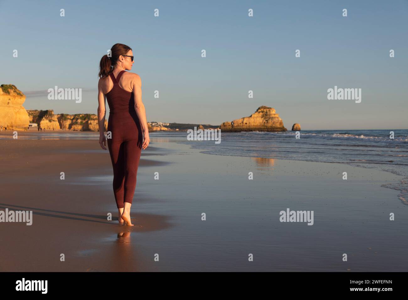 Donna sportiva che cammina a piedi nudi lungo la spiaggia Foto Stock